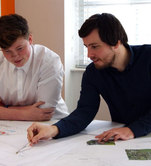  A man pointing towards a drawing off a sitemap, while another man watches intently.