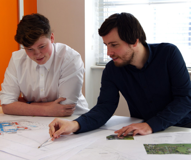  A man pointing towards a drawing off a sitemap, while another man watches intently.