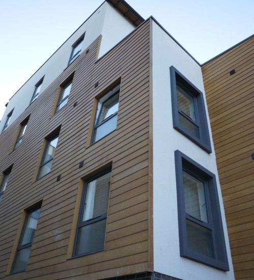  A photo of the corner of a building with a mix of wooden panels on one side of the building and white painted