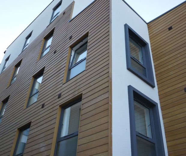  A photo of the corner of a building with a mix of wooden panels on one side of the building and white painted