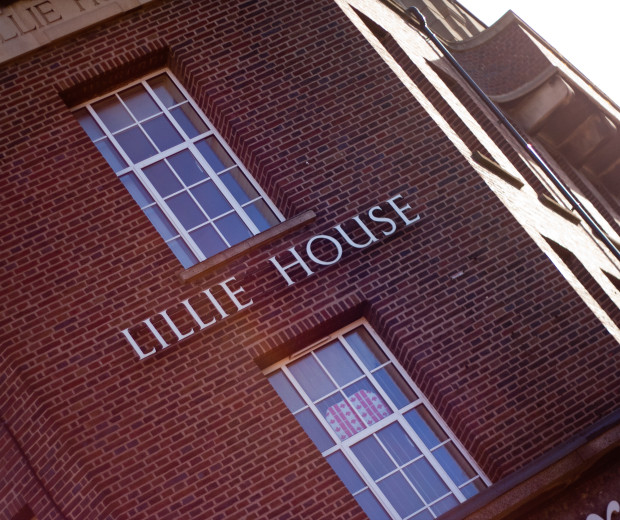 A photo of a large building with red bricks. Between two large vertical windows are the words Lillie House